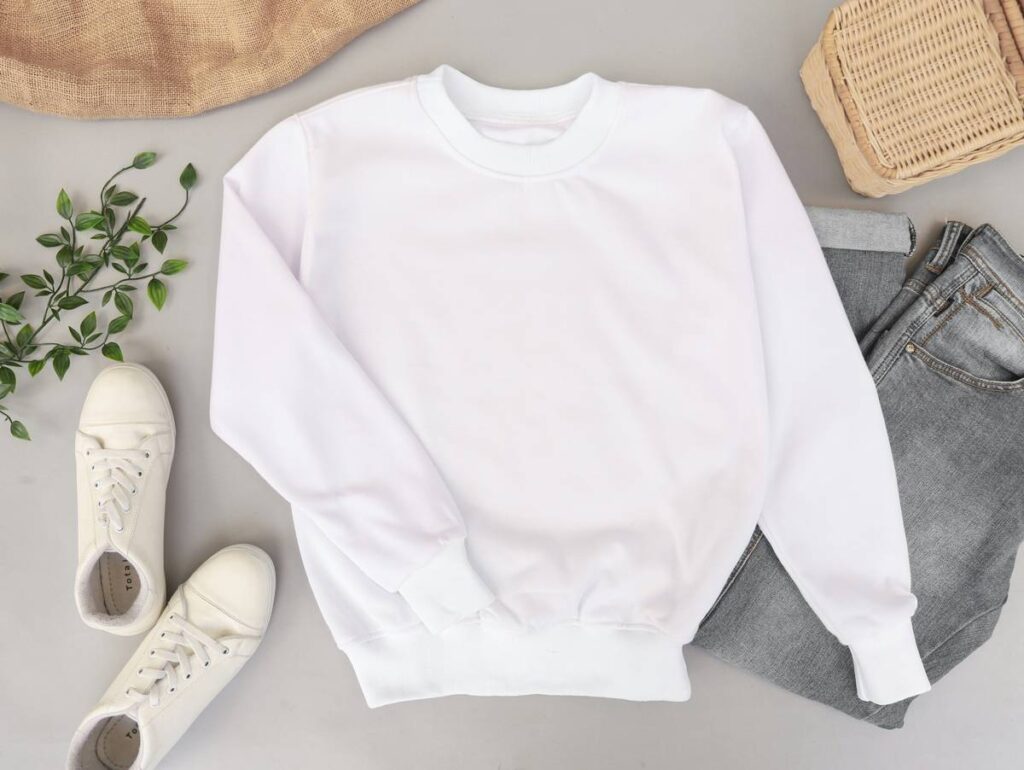 Blank and plain white sweater mockup photo with jeans and sneakers on the background. Use it to display your apparel design.