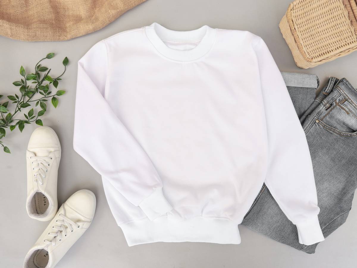 Blank and plain white sweater mockup photo with jeans and sneakers on the background. Use it to display your apparel design.